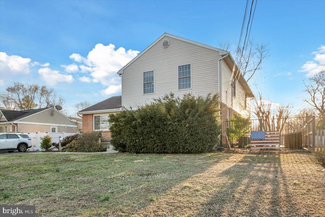 view of home's exterior featuring brick siding, a lawn, and fence