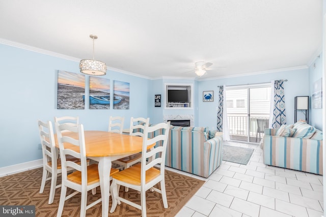 dining space featuring ornamental molding, a fireplace, a ceiling fan, and baseboards