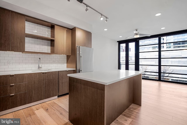 kitchen featuring a sink, stainless steel refrigerator, decorative backsplash, expansive windows, and open shelves