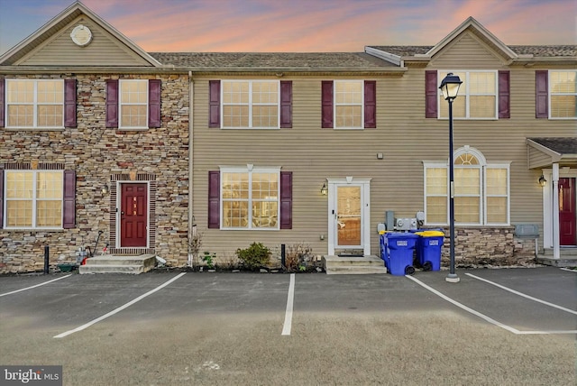 townhome / multi-family property featuring uncovered parking, entry steps, and stone siding