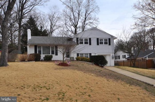 split level home featuring driveway, a front lawn, a chimney, and fence