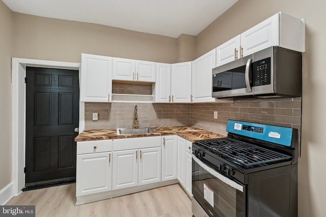 kitchen with light wood finished floors, appliances with stainless steel finishes, a sink, and white cabinets