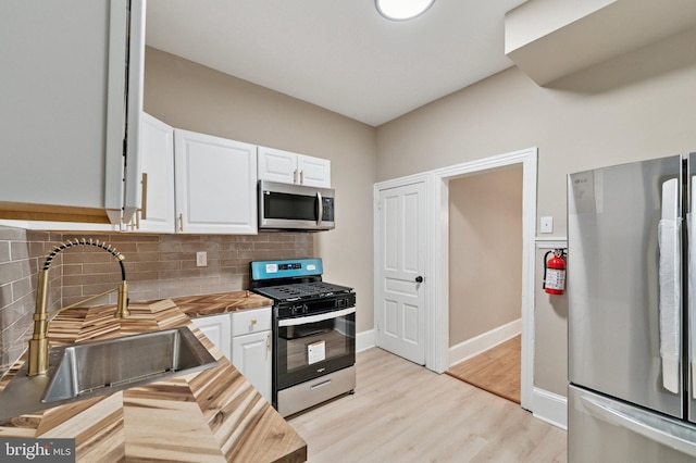 kitchen with tasteful backsplash, butcher block counters, appliances with stainless steel finishes, white cabinetry, and a sink