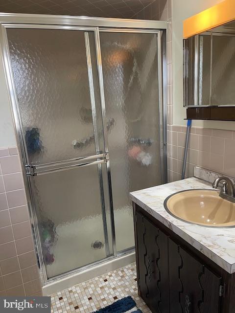 bathroom with tile patterned flooring, a shower stall, tile walls, and vanity