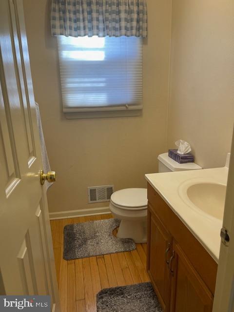 half bathroom with toilet, wood finished floors, vanity, visible vents, and baseboards