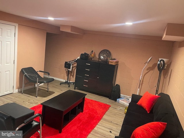 living area with wood finished floors, concrete block wall, and recessed lighting