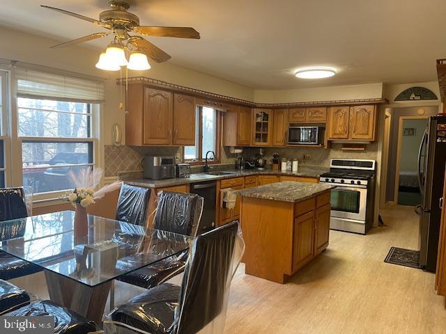 kitchen featuring stainless steel appliances, a sink, brown cabinets, a center island, and tasteful backsplash