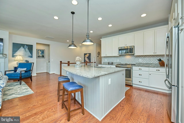 kitchen featuring stainless steel appliances, light wood-type flooring, decorative backsplash, and white cabinets