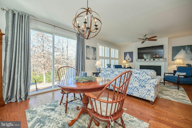 dining area featuring ceiling fan with notable chandelier, a fireplace, and wood finished floors