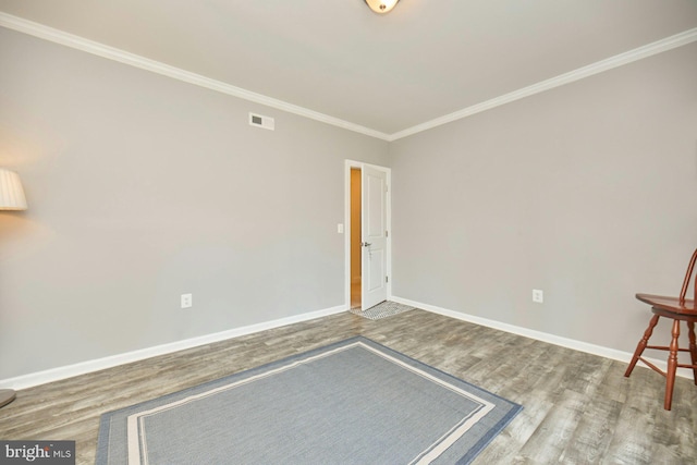 interior space with crown molding, wood finished floors, visible vents, and baseboards