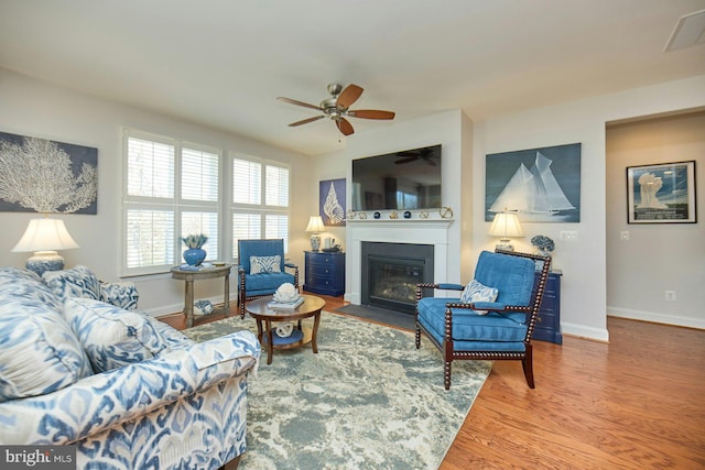 living room featuring a fireplace with flush hearth, visible vents, baseboards, and wood finished floors