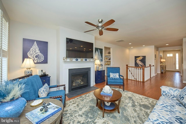 living room with built in shelves, recessed lighting, visible vents, a fireplace with flush hearth, and wood finished floors