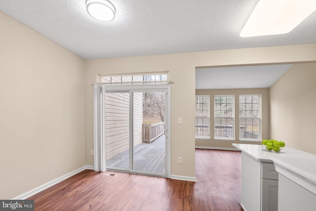 unfurnished dining area featuring visible vents, a textured ceiling, baseboards, and wood finished floors