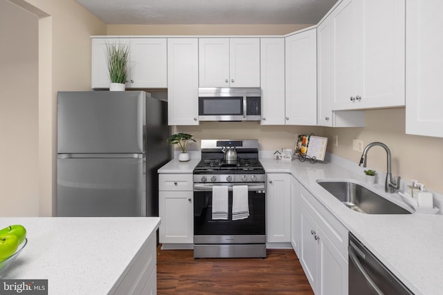 kitchen with appliances with stainless steel finishes, dark wood-type flooring, white cabinets, a sink, and light stone countertops