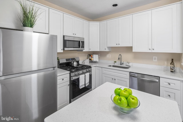 kitchen with light stone countertops, white cabinetry, stainless steel appliances, and a sink