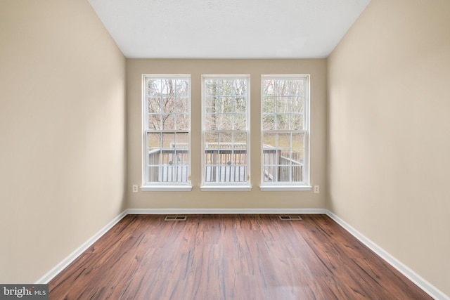 empty room with dark wood-style floors, visible vents, and baseboards