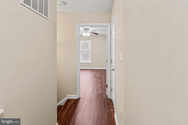 hall with visible vents, a textured ceiling, baseboards, and wood finished floors