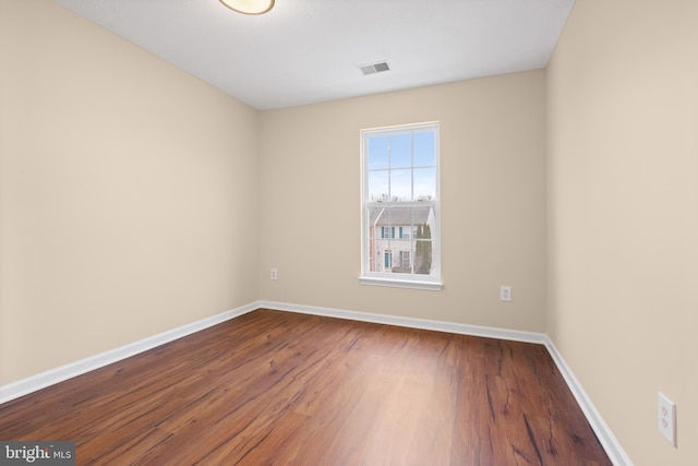 unfurnished room with baseboards, visible vents, and dark wood finished floors