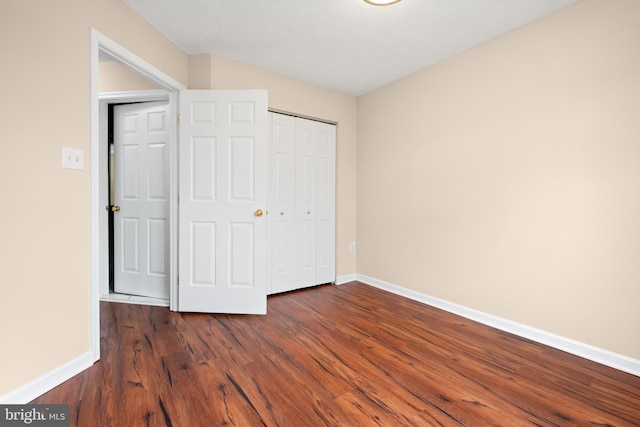 unfurnished bedroom featuring a closet, dark wood finished floors, and baseboards