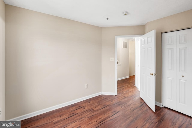 unfurnished bedroom with visible vents, a closet, baseboards, and dark wood-type flooring