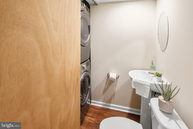 clothes washing area featuring laundry area, baseboards, stacked washer / drying machine, and wood finished floors