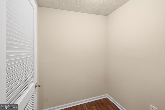 unfurnished room featuring a textured ceiling, dark wood finished floors, and baseboards