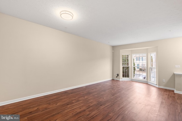 spare room with a textured ceiling, baseboards, and dark wood-style flooring