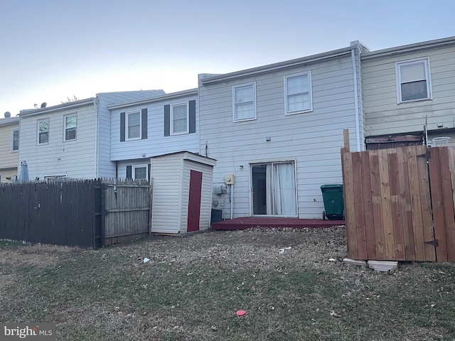 back of house with fence, a storage unit, and an outbuilding