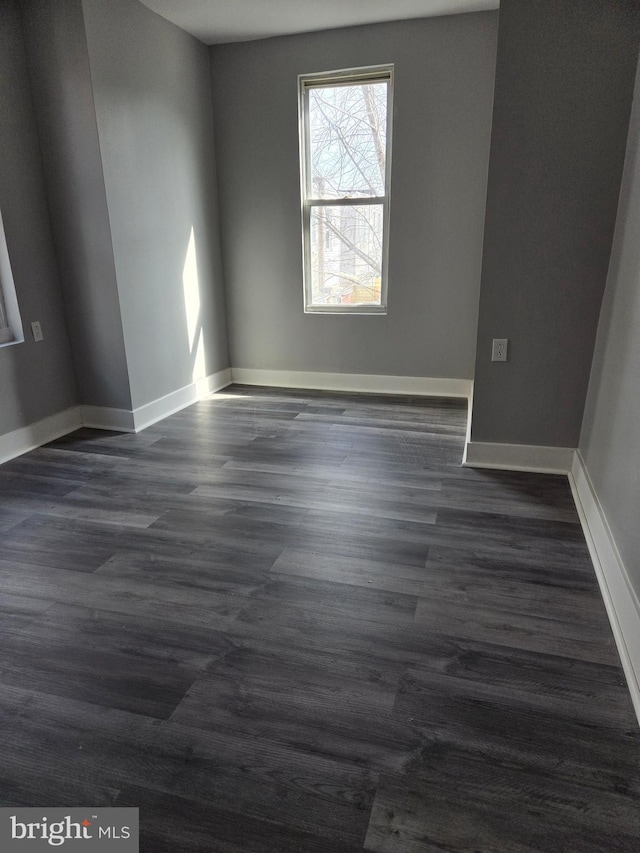 empty room with dark wood-type flooring and baseboards