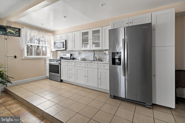 kitchen with light tile patterned floors, decorative backsplash, glass insert cabinets, appliances with stainless steel finishes, and white cabinetry