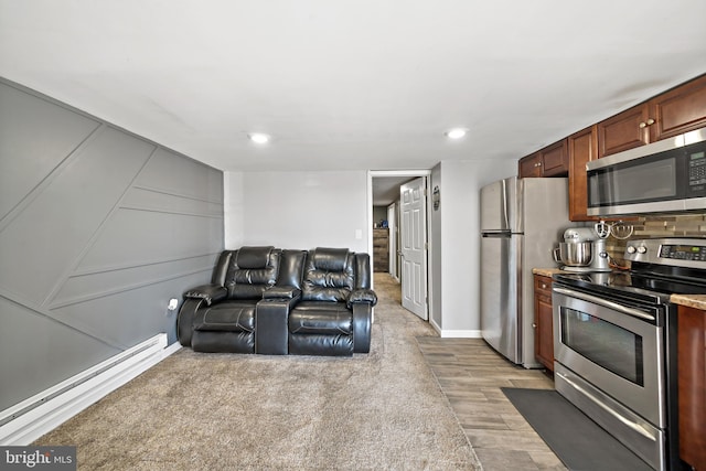 kitchen featuring a baseboard radiator, appliances with stainless steel finishes, open floor plan, light wood-style floors, and a decorative wall