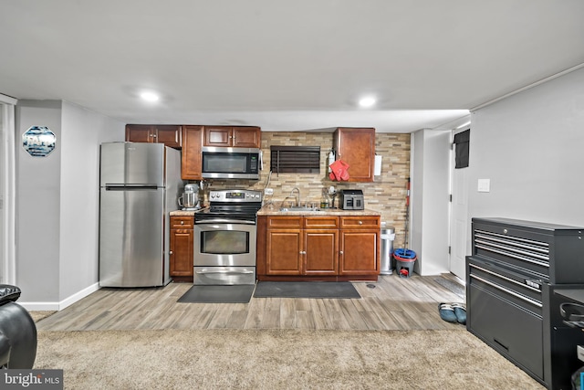 kitchen with light wood-type flooring, appliances with stainless steel finishes, a sink, and light colored carpet