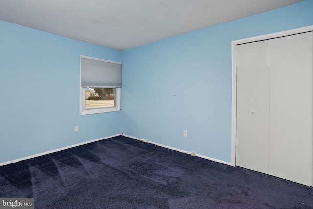 unfurnished bedroom with a closet, dark carpet, and baseboards