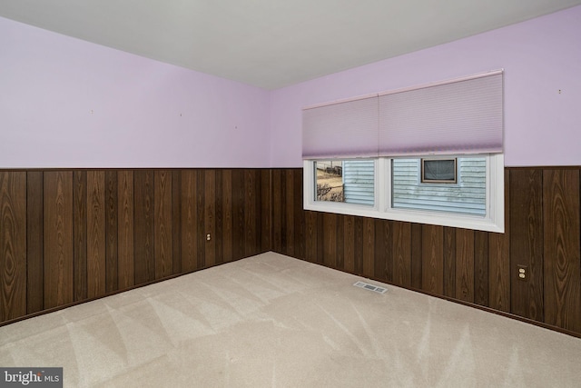 carpeted spare room with a wainscoted wall, visible vents, and wooden walls