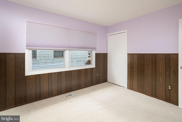 carpeted spare room with a wainscoted wall, wood walls, and visible vents