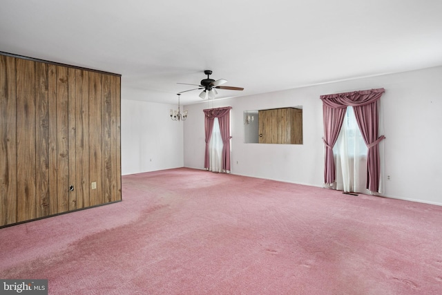 empty room with carpet floors, wooden walls, and ceiling fan with notable chandelier