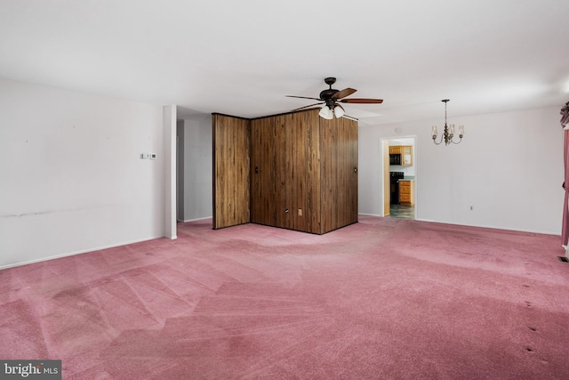 carpeted spare room with ceiling fan with notable chandelier and baseboards