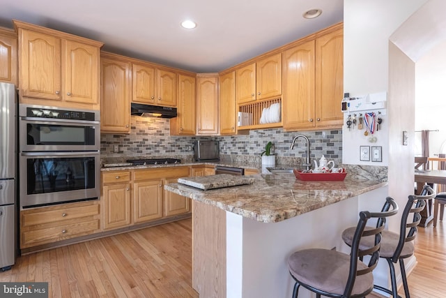 kitchen featuring light stone countertops, under cabinet range hood, a kitchen breakfast bar, stainless steel appliances, and a sink