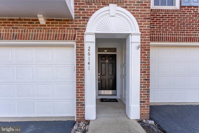 property entrance featuring brick siding, an attached garage, and aphalt driveway