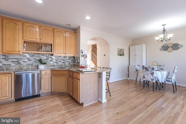 kitchen with light wood finished floors, backsplash, dishwasher, light stone counters, and a sink