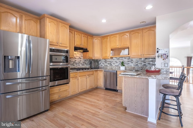 kitchen featuring a peninsula, light wood-style flooring, light stone counters, and appliances with stainless steel finishes