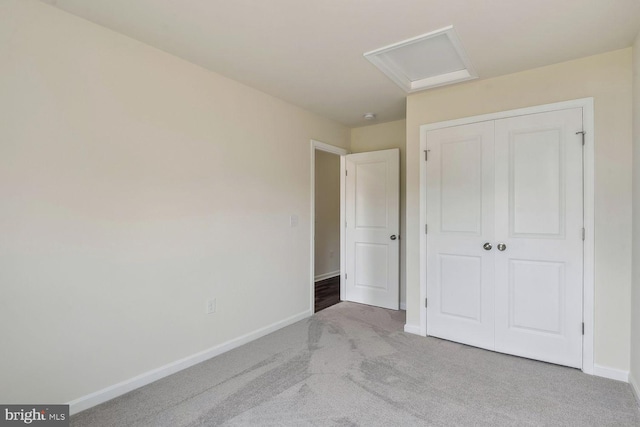 unfurnished bedroom with attic access, carpet, a closet, and baseboards