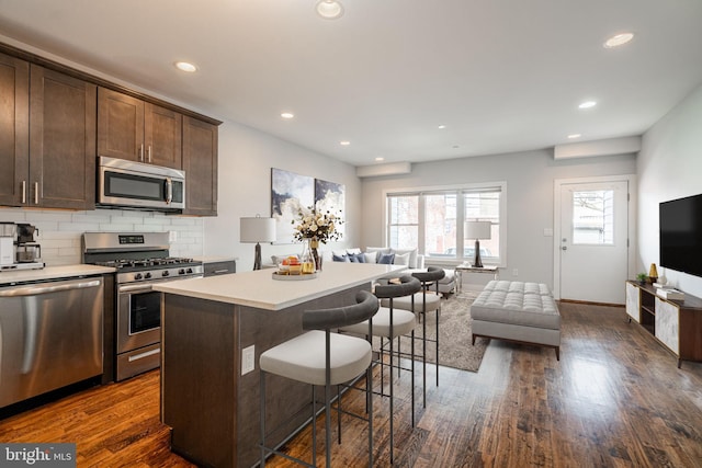 kitchen with dark wood-style floors, a breakfast bar, stainless steel appliances, decorative backsplash, and open floor plan