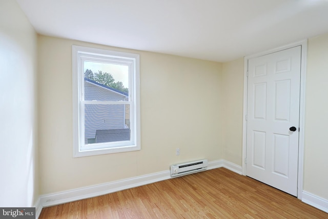 spare room featuring baseboard heating, light wood-type flooring, and baseboards