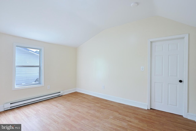 spare room featuring a baseboard heating unit, vaulted ceiling, baseboards, and wood finished floors