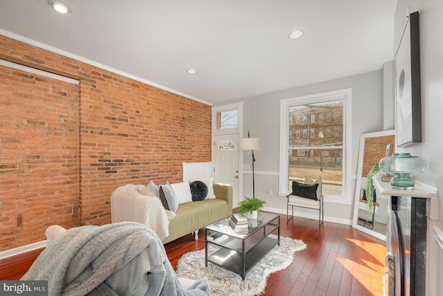 living area with recessed lighting, baseboards, hardwood / wood-style floors, and brick wall