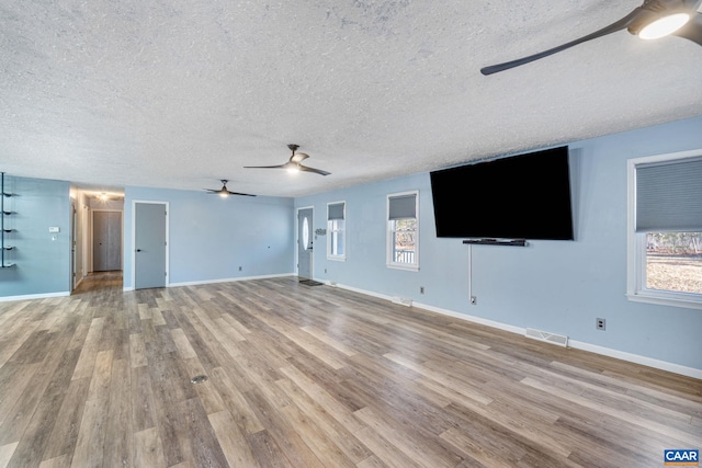 unfurnished living room featuring baseboards, a textured ceiling, visible vents, and wood finished floors