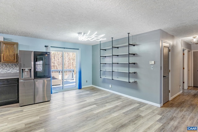 interior space featuring a textured ceiling, baseboards, light wood-type flooring, stainless steel refrigerator with ice dispenser, and decorative backsplash