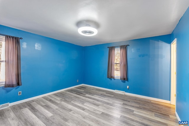 spare room with wood finished floors, visible vents, and baseboards