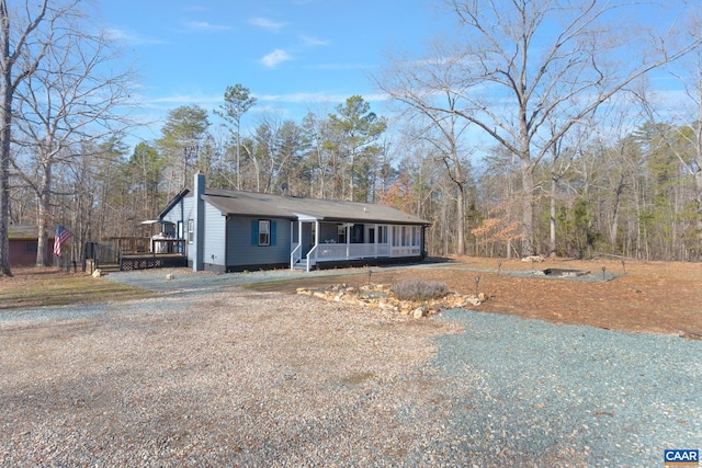 view of front of property with covered porch, a chimney, and gravel driveway